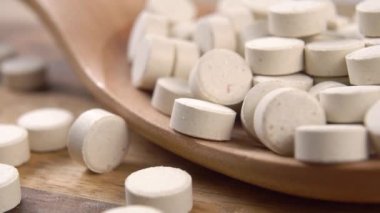 Bitkisel yuvarlak gıda takviye hapları. Bira mayası ve buğday tohumu. Hapları yavaş çekimde tahta kaşığa düşürmek. Makro. Kırsal biçim