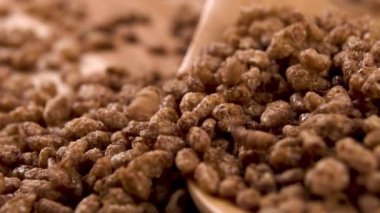 Çikolatalı gevrek pirinç, ahşap bir masada tahta bir kaşığa düşer. Makro. Gevrek, tatlı, gevrek kahvaltı. Yavaş çekim.