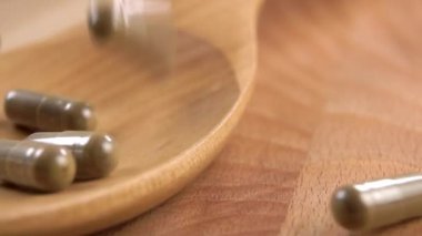 Ashwagandha bitkisel kapsülleri yavaş çekimde tahta bir kaşığa düşer. Makro atış. Şifalı bitki takviyesi.