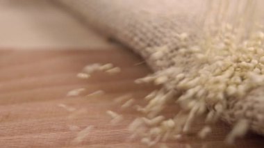 Çiğ organik kinoa tohumları eski ahşap bir masanın üzerine katlanmış kaba bir çuval bezine düşer. Makro. Dolly vurdu. Kırsal biçim