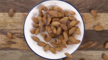 Kurutulmuş çiğ badem fıstığı kırsal bir mutfak tahtasındaki bir tabağa düşer. Üst Manzara. Yakın plan. Yavaş çekim