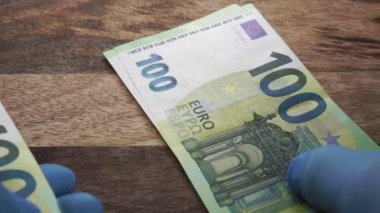 Euro paralarını sayıyorum. Tıbbi mavi eldivenli eller, ahşap bir masanın üzerine banknotlar sererler. İş sağlığı konsepti