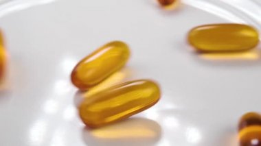 Omega-3 balık yağı sarı kapsüller yavaş çekimde beyaz bir tabağa düşüyor. Kapatın. İlave haplar