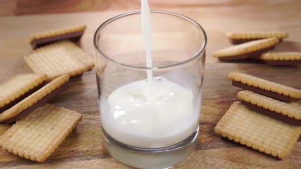全脂牛奶倒入木制桌子上的杯子里 桌上放着有花纹的脆饼干 慢动作靠近点 — 图库视频影像