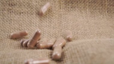 Kahverengi tıbbi bitkisel kapsüller kaba bir çuval bezi üzerine düşer. Kapatın. Yavaş çekim