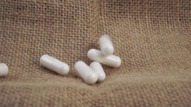 Beyaz tıbbi iyileştirme kapsülleri ağır çekimde kaba kaba kaba kaba kaba bir çuval bezi üzerine düşer. Yakın plan. Sağlık hizmeti kavramı