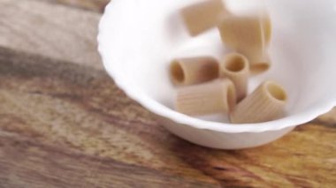 Yavaş çekimde beyaz bir kasede beyaz bir masada kuru rigatoni italyan makarnası düşmek. Geleneksel mutfak konsepti