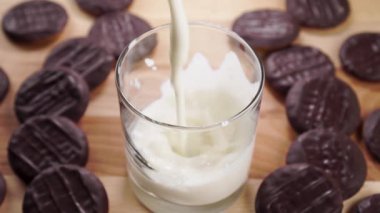 Bir bardak taze yoğurt ve çikolatalı kurabiyeler. Ağır çekimde kalın kefir dökülüyor. Yakın plan.