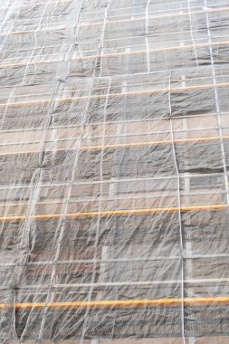 İskeleli bir binanın ön cephesinde koruyucu bir güvenlik ağı olan bir inşaat alanı. Eski konut yenileme konsepti. Dikey görünüm