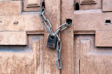 Eski bir ahşap kapının üzerindeki zincirin üzerindeki paslı siyah asma kilit. Yakın plan. Giriş yasak bir kavramdır.