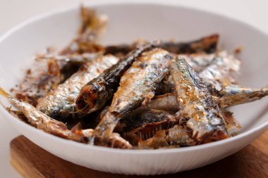 Fried sardine fish in white plate on wooden kitchen board close-up