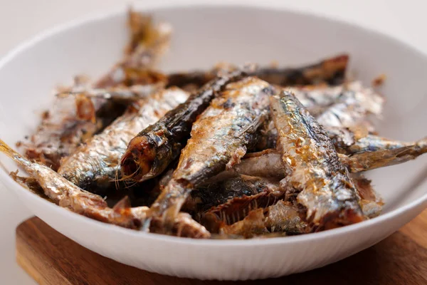 Fried sardine fish in white plate on wooden kitchen board close-up