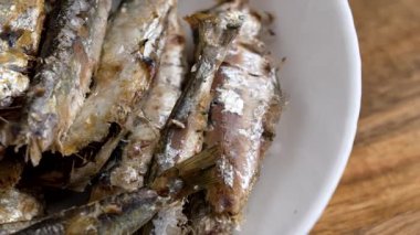 Mutfak masasında beyaz bir seramik kasede pişmiş sardalya.