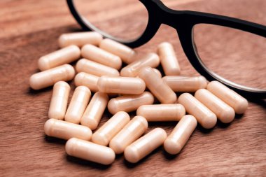 Dağıtılmış bej ilaç kapsülleri siyah gözlüklü ahşap masanın üzerinde. Reçeteli tedavi kavramı