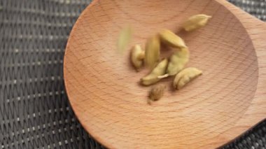 Kurutulmuş kakule baharatı ve tohum kapsülleri yavaş çekimde tahta kaşığa dökülüyor. Üst görünüm
