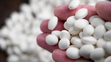 Beyaz vitamin hapları, insan elinden ahşap bir kasenin içindeki tabletlerin üzerine ağır çekimde dökülüyor. Besin takviyesi kavramı