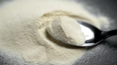 Süt tozu, siyah seramik bir tabağın üzerine paslanmaz çelik bir kaşık yığılmış. Yüksek protein uygunluk takviyesi. Atletik diyet konsepti. Döndürme