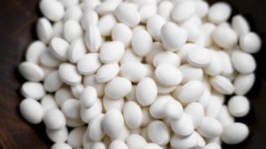 Beyaz kolajen hapları ağır çekimde ahşap bir kabın içine düşüyor. Üst görünüm.