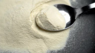 Sütlü protein dolu metal kaşık siyah seramik tabağa odaklan. Pudralanmış spor beslenme bileşeni