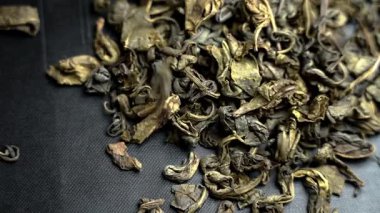 Kurumuş Çin yeşil çay yaprakları yavaş çekimde koyu arkaplana düşüyor. Geleneksel doğulu içecek malzemesi