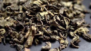 Koyu dokulu arka planda gevşek yapraklı Çin yeşil çayı. Geleneksel Asya içecek malzemesi ve kıvrımlı kuru yapraklar. Döndürme