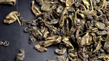 Siyah karton ambalaj kutusunun yüzeyinde dağınık yeşil çay yaprakları yığını.