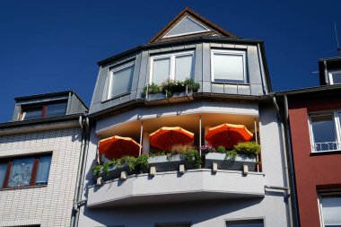 Köln 'ün öğrenci bölgesinde modern mimari çarpıcı simetri, açık mavi gökyüzü ve üç belirgin turuncu güneş şemsiyesi içerir.