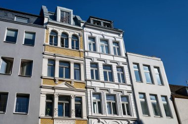 Açık mavi gökyüzü altında modern binaların yanında sarı tuğlalı bir tarihçi cephesinin yer aldığı zıt mimari tarzlara düşük açılı bakış açısı