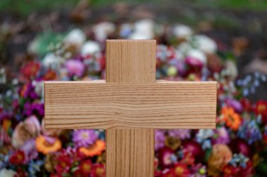 Sade, ahşap bir haçın yakın planında renkli cenaze çiçekleri bulanıklaşıyor. İnanç, kayıp ve diriliş kavramı