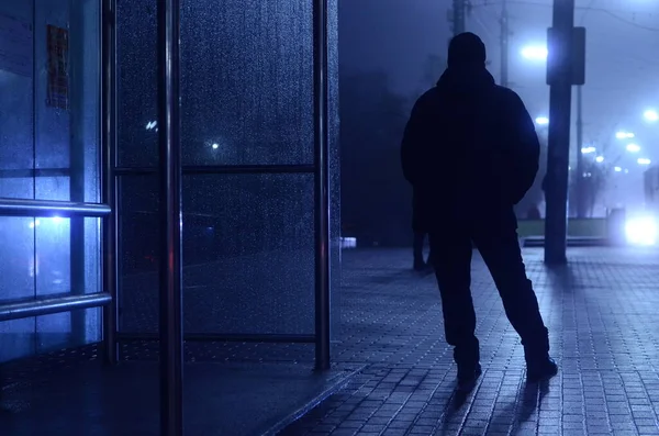 man walking by glass bus stop at night