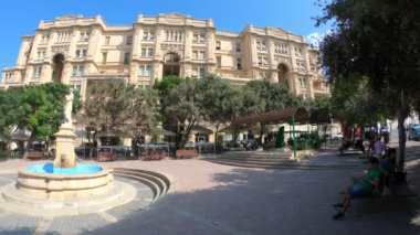 İnsanlar bankta ve çeşmenin yanındaki sokak kafesinde. 