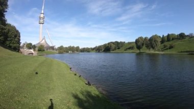 Havuzu, ağaçları ve mavi bulutlu gökyüzünün altında kulesi olan yemyeşil bir park sahnesi