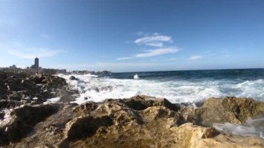 Dalgalar parlak güneş ışığında mavi gökyüzünde yuvarlanıyor.