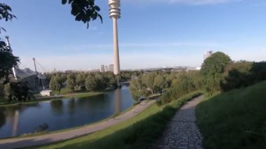 Havuzu, binaları ve mavi bulutlu gökyüzünün altındaki kulesi olan yemyeşil park manzarası
