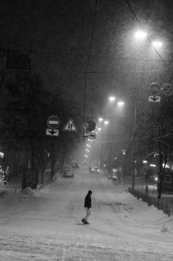 Karlı Kyiv Caddesi 'nden geçen adam gece aydınlandı, siyah ve beyaz.