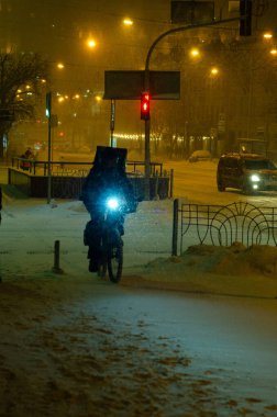 Bisikletli teslimatçının karlı akşam sokağında yürüdüğü dikiz görüntüsü