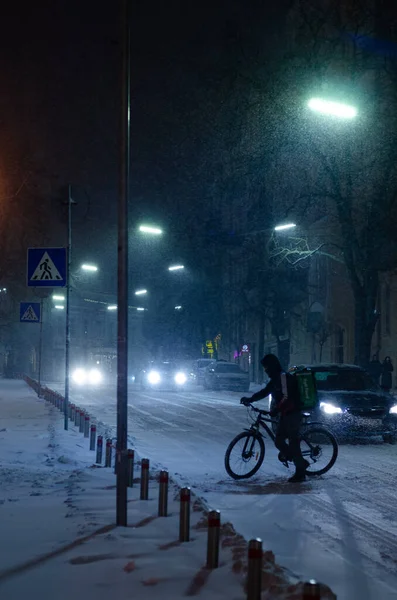 person on bicycle at snowy night street with cars