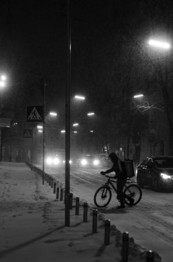 Karlı gece caddesinde siyah beyaz arabalı bisikletli biri.
