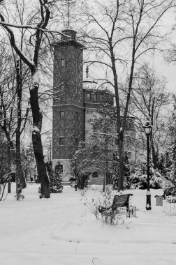 old tower and bench in park covered in snow, black and white