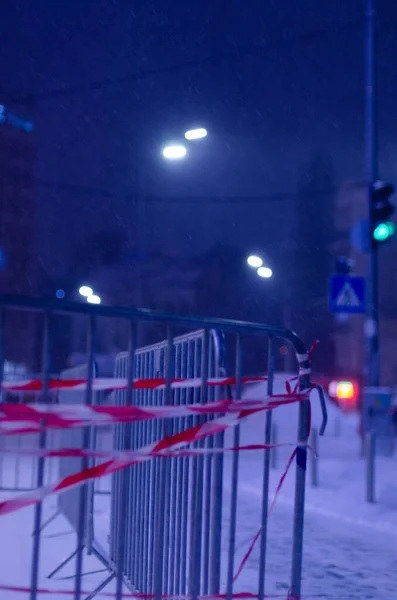 metal fence with guard tape on snowy street at night