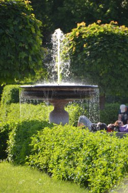 fountain in sunny green park with people on background