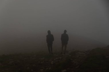 Sisin içinde tepede duran iki kişinin siluetleri.