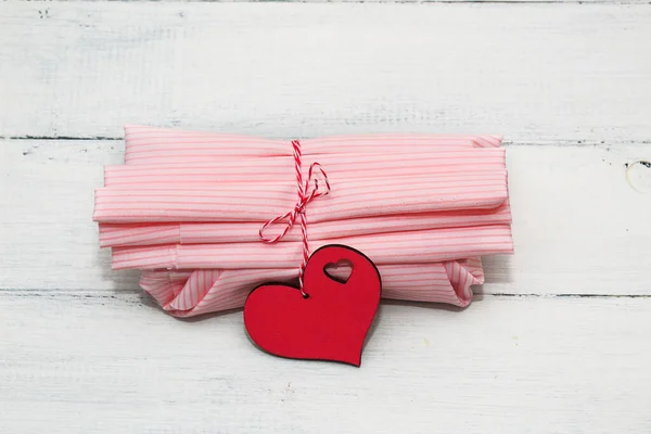 Wrapping gift for Valentine\'s Day, Birthday, Mother\'s Day using pink cotton textile and hearts decor on a white wooden background. Furoshiki, ecological gift wrapping