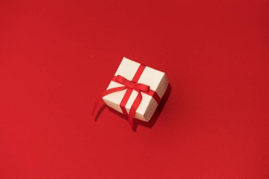 Kırmızı arka planda kırmızı kurdeleli beyaz hediye kutusu. Valentins Günü kavramı, boşluğu kopyala ve taklit et