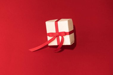 Kırmızı arka planda kırmızı kurdeleli beyaz hediye kutusu. Valentins Günü kavramı, boşluğu kopyala ve taklit et
