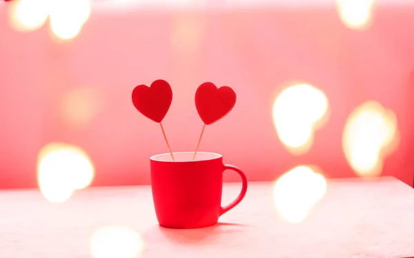Röda trähjärtan i en röd kopp på en rosa bakgrund med kopieringsutrymme. Alla hjärtans dag gratulationskort med mjuk bokeh — Stockfoto