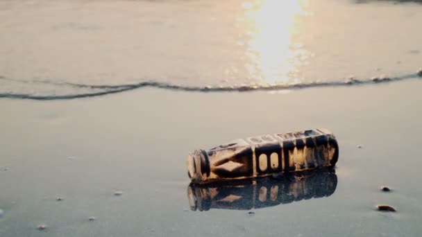 日没時にビーチで波に洗われたペットボトルからのゴミ — ストック動画