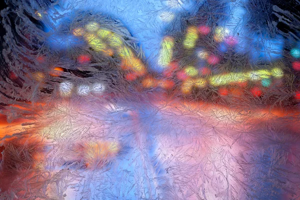 Lumières multicolores de la ville derrière le verre givré avec des motifs givrés Image En Vente