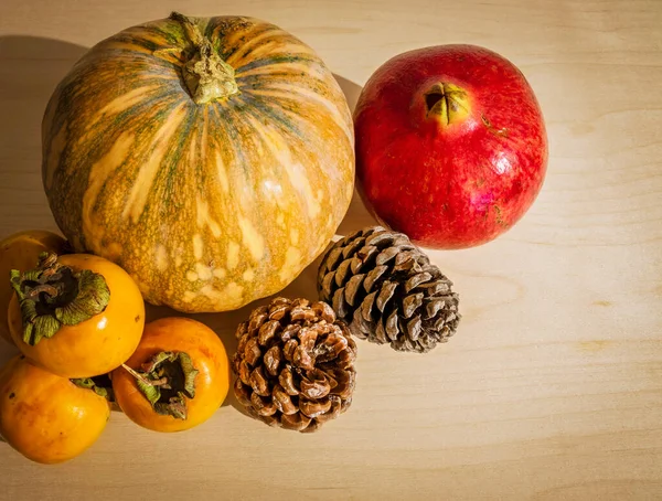 winter fruits and vegetables on a wooden floor. Pomegranate, pumpkin, persimmon and pine cones. Christmas and winter holidays. Close-up and white background.