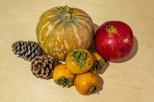 winter fruits and vegetables on a wooden floor. Pomegranate, pumpkin, persimmon and pine cones. Christmas and winter holidays. Close-up and white background.